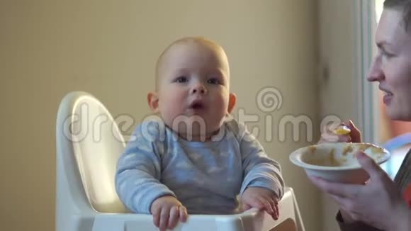 先喂宝宝妈妈用一个高孩子的椅子蔬菜泥喂她的孩子婴儿食品视频的预览图