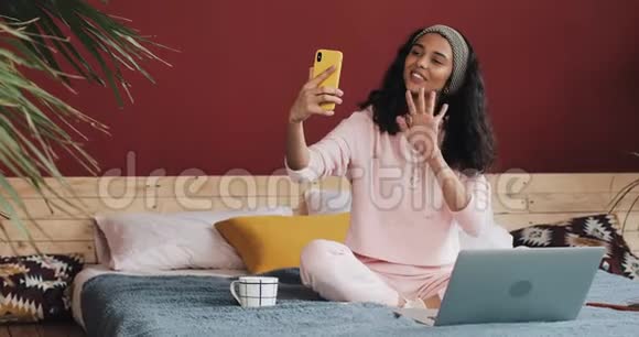 快乐的非裔美国女孩坐在homec的床上和她的朋友们一起在视频中打她的黄色电话视频的预览图
