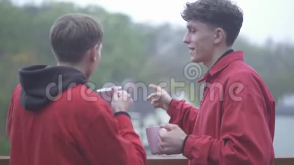两个穿红色夹克衫的年轻人喝着咖啡杯微笑着朋友一起在户外玩耍视频的预览图