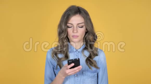 黄色背景下的年轻女孩在智能手机上交谈视频的预览图
