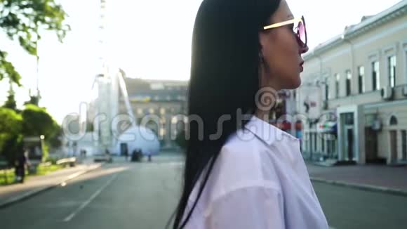 美丽的深色头发戴着时尚太阳镜慢动作地走在城市街道上视频的预览图