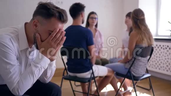 小组治疗悲伤的男人用双手捂住脸周围坐在椅子上的人的背景视频的预览图