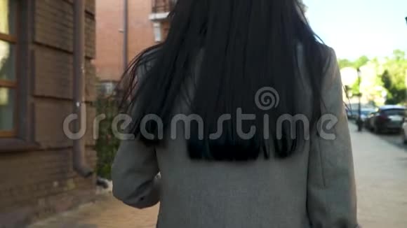 身着灰色外套的长发黑发女子在城市大街上散步视频的预览图