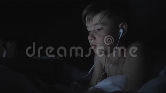 一个晚上在智能手机上的男孩在床上看视频电影后期评论视频的预览图