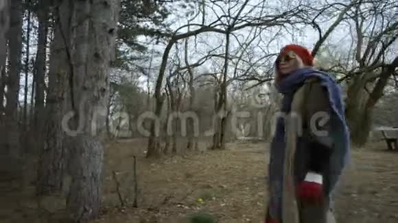 年轻漂亮的女人戴着红帽子在森林中漫步触摸着树视频的预览图