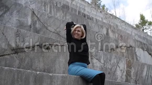 年轻的金发女孩坐在大理石采石场的台阶上微笑着视频的预览图