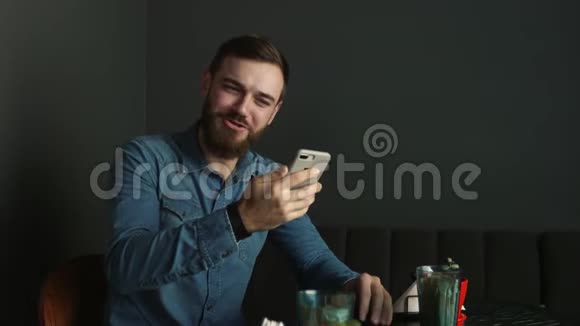 咖啡馆里留着胡子的年轻人的肖像蓝衫男用视频通话视频的预览图