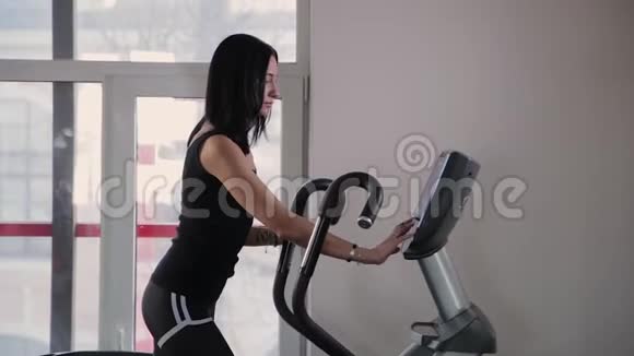 漂亮的运动年轻女孩在健身房的椭圆教练上做设置视频的预览图