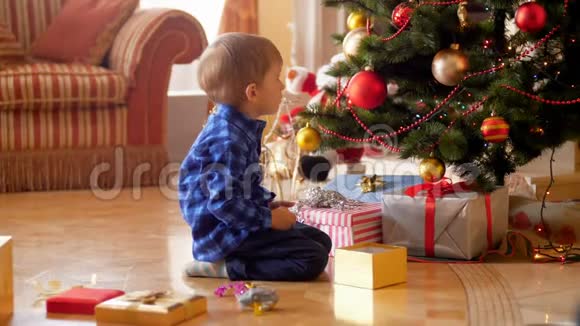 3岁的小男孩坐在客厅的地板上看着装饰好的圣诞树视频的预览图