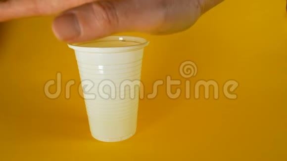 一个男人他的手在黄色的背景上捏碎一个白色的一次性塑料杯这是生态和其他主题的理想素材视频的预览图