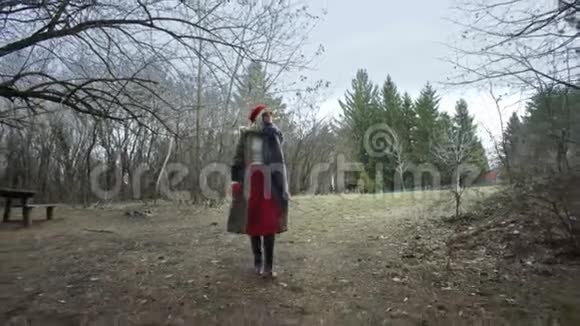 年轻漂亮的女人戴着红帽子在森林中漫步触摸着树视频的预览图
