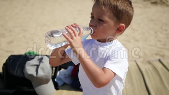 一个小孩在沙滩上喝塑料透明瓶子里的水视频的预览图