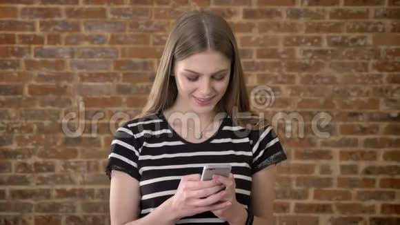 年轻可爱的金发女郎正在智能手机上输入信息梦想概念沟通概念砖背景视频的预览图