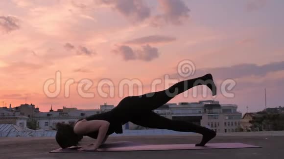 夏天日落时分Yogi女孩站在屋顶上一条腿朝下的狗健康的生活方式放松的概念视频的预览图