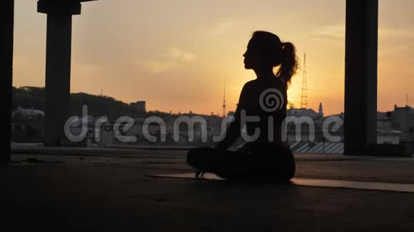 Yogi女孩坐在莲花的姿势下在日落时分在夏天废弃的建筑物里改变它健康的生活方式运动视频的预览图