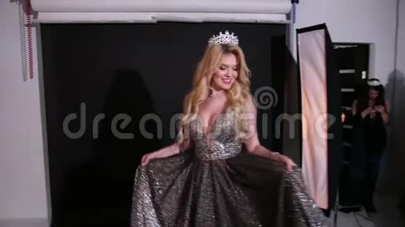 女孩金发模特穿着闪亮的连衣裙戴着皇冠在工作室拍照视频的预览图