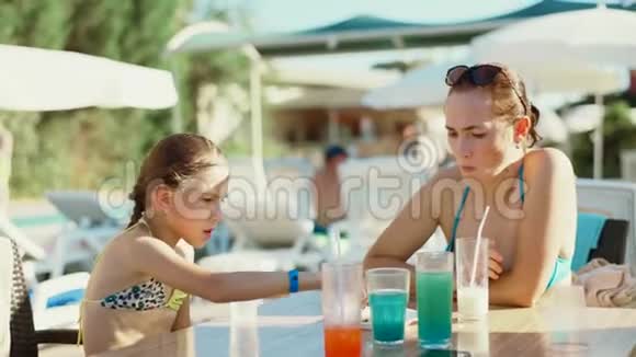 一个女人和她的女儿穿着泳衣在游泳池酒吧附近的一张桌子上吃午饭视频的预览图