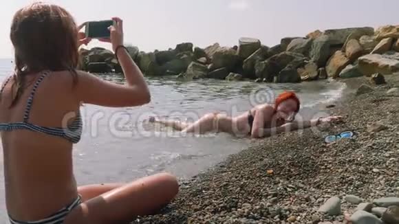 金发美女在鹅卵石滩的海水中拍摄红发照片视频的预览图