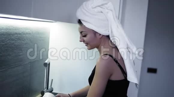 美丽微笑的年轻女子头上戴着白色浴巾在厨房洗碗家庭中的年轻妇女视频的预览图