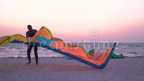 一个穿着潜水服的男人手里拿着一只训练风筝沿着海滩走着慢动作视频的预览图