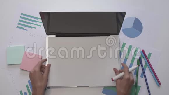 女人在笔记本电脑上的一张纸上写视频带有图表的办公桌面视频的预览图