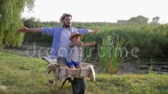 对家庭来说很有趣父亲和儿子想象他们像飞机一样坐在农村的手推车里视频的预览图
