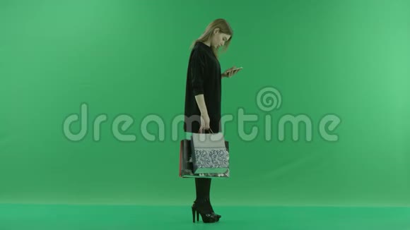 漂亮的年轻女性在手里拿着袋子购物后在智能手机上发短信颜色键绿色背景视频的预览图