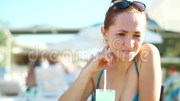 年轻的女士穿着比基尼和太阳镜在海滩酒吧喝鸡尾酒一个女人在餐桌旁视频的预览图