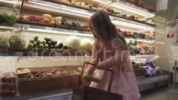 可爱的小女孩把蔬菜和水果放在超市的篮子里视频的预览图
