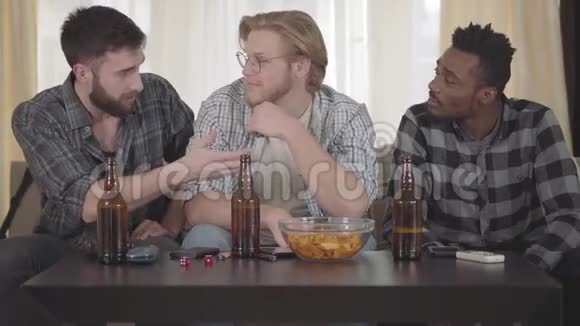 两个白种人和一个非裔美国人坐在沙发上的肖像三个男人坐在家里喝酒视频的预览图
