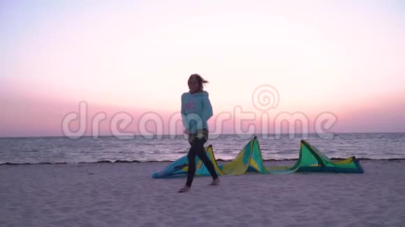 一个穿着潜水服的女人在黎明时分沿着海滩散步经过训练风筝视频的预览图