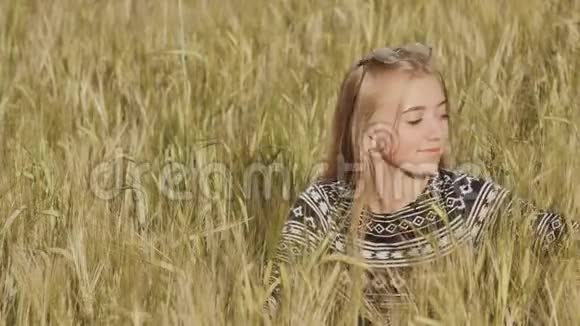 美丽的金发少女坐在麦田里微笑视频的预览图