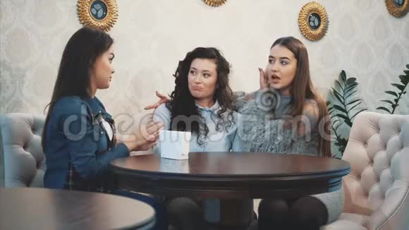 三个可爱的漂亮女孩坐在咖啡馆里在这期间他们聊天直接在眼睛里看到漂亮的黑色长发视频的预览图