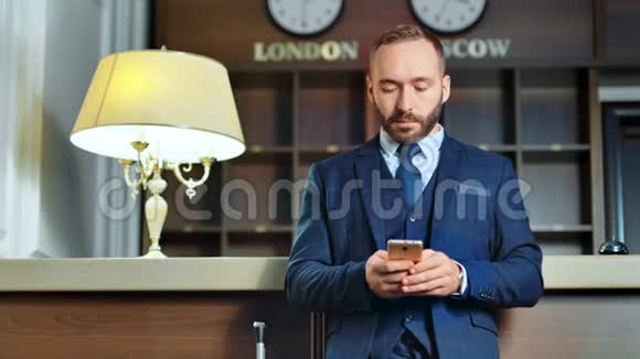 时尚的男性商人在酒店前台使用智能手机写信息视频的预览图