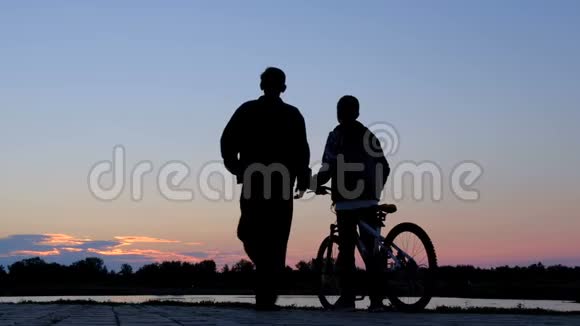 一名男子和一名少年骑着一辆自行车在清晨的天空中拍摄的剪影视频的预览图