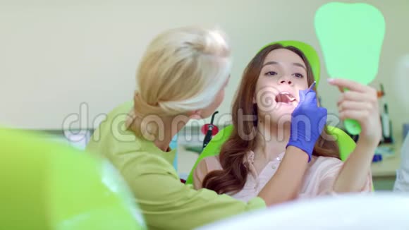 年轻女子在牙医椅上看镜子女牙医治疗病人视频的预览图