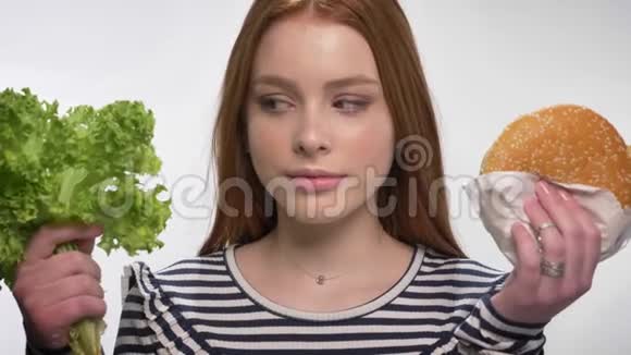 年轻的生姜女孩选择健康和不健康的食物选择生菜白色背景视频的预览图