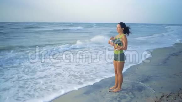 早上慢跑后美丽的女人站在海边喝着水视频的预览图
