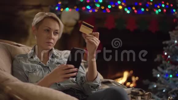 成年金发短毛妇女在圣诞夜使用智能手机和信用卡在线购物视频的预览图