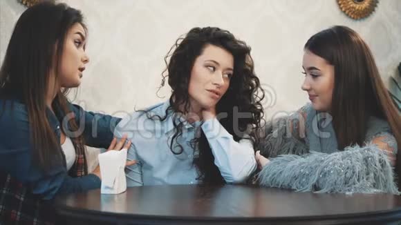 三个可爱的漂亮女孩坐在咖啡馆里在这期间他们聊天直接在眼睛里看到漂亮的黑色长发视频的预览图