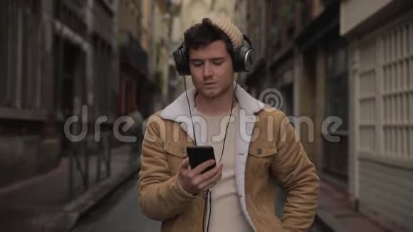 笑容可掬帅哥戴着耳机用智能手机听音乐在老城街头跳舞视频的预览图