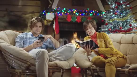 圣诞节晚上帅哥在智能手机上发短信而女人在看书视频的预览图