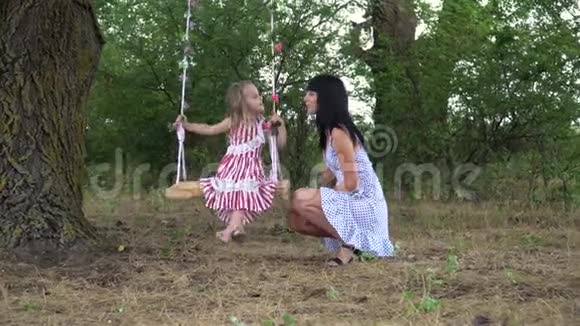 美丽的小女孩和她的母亲骑在秋千上在公园里在大自然中视频的预览图