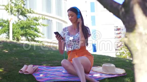 城市野餐年轻漂亮的女人在耳机里听音乐跳舞视频的预览图