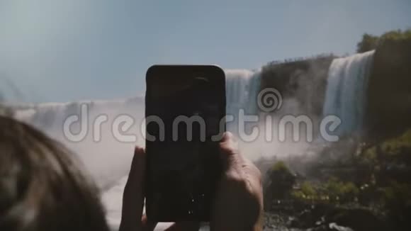 慢动作特写镜头人类双手捧着黑色智能手机拍摄史诗般的尼亚加拉大瀑布风景视频的预览图