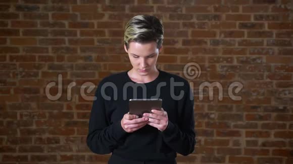 美丽的白种人妇女使用她的平板电脑和微笑迷人的相机砖背景隔离视频的预览图