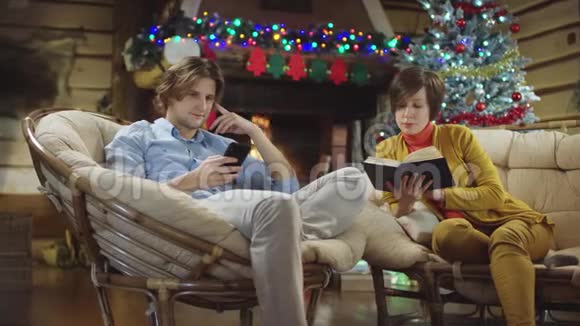 年轻人在智能手机上上网而他的母亲在圣诞夜看书视频的预览图