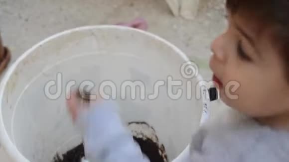 两岁的男孩在玩白色桶里的泥土视频的预览图
