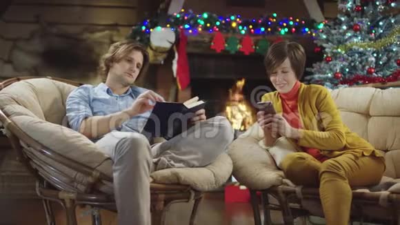 年轻人在圣诞节晚上当他的母亲在手机上上网时正在看书视频的预览图