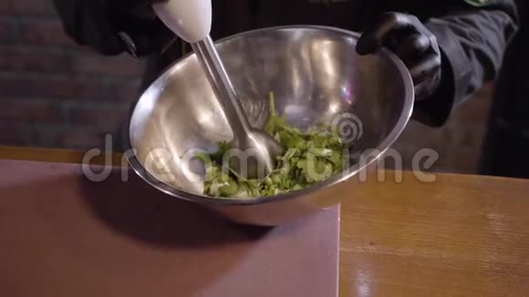 厨师手中的黑色橡胶厨师手套搅拌奶油与欧芹使用搅拌机在大铝碗关闭视频的预览图